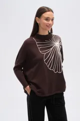 Sweater de tejido marrón oscuro con cuello alto y un gran aplique bordado en blanco con diseño abstracto que simula un abanico o flor.