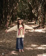 Sweater color crema de tejido de punto con cuello redondo y mangas largas. Presenta un arcoíris bordado a mano en el frente.