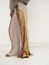 Pantalón de brocato color champagne con lentejuelas doradas en los laterales, tiro medio, cuatro bolsillos, cierre frontal con botón de guampa y bajo acampanado con tajos laterales.