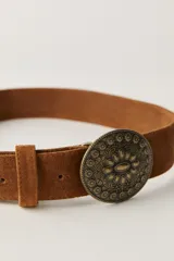 Cinturón de ante negro con hebilla metálica ovalada de estilo western, con diseño grabado de flores y detalles ornamentales.