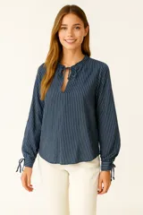 Blusa azul con rayas verticales blancas, cuello mao con lazo y mangas largas abullonadas con puños elásticos.