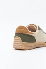 Zapatilla urbana de mujer con silueta retro, combinando paneles de gamuza marrón oscuro y material color crema en el cuerpo. Presenta detalles en color bordó en el talón y cordones beige. La suela es robusta de color marrón claro con relieve.