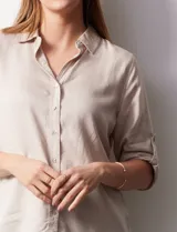 Camisa color beige de tencel, marca Hester & Orchand. Cuello con solapa, escote en V y abertura central con botones. Delantera con bolsillos. Largo de manga regulable con presilla y botón.