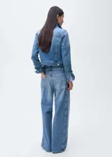 Chaqueta de jean celeste con cuello camisero, cierre frontal con botones metálicos, dos bolsillos de parche con solapa en el pecho y mangas largas con puños abotonados.