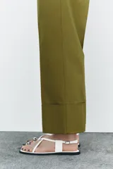 Pantalón color beige de corte ancho, con tiro medio, trabillas en la cintura y raya planchada.