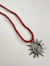 Collar con dije plateado en forma de sol con espiral en el centro y cordón rojo.