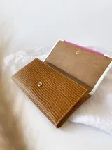 Billetera de cuero con estampado reptil en color marrón y fucsia con detalles en blanco. Tiene un sistema de cierre con broche y monedero externo.