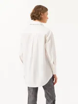 Camisa celeste de poplin, corte clásico, largo a la cadera y mangas largas. Cuello con detalle de piedras engarzadas. Cierre frontal con botones de pasta al tono.