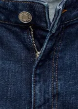 Pantalón de jean azul oscuro, de tiro medio, corte flare y terminación desflecada.