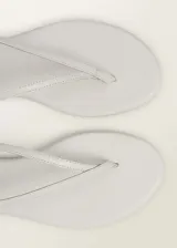 Sandalia plana blanca de cuero caprino con diseño de tiras y cierre de tira con hebilla.