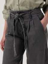 Pantalón de jeans tiro alto, color gris oscuro lavado, de corte recto y ancho. Presenta pliegues frontales y pretina ajustable con lazo.