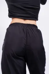 Pantalón negro de acetato con cintura elástica y cordón ajustable. Presenta una franja blanca a lo largo de la pierna.