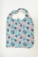 Tote bag de tela con estampado de hojas de palmera en tonos azul, celeste y rosa. Tiene doble asa superior y cierre con botón a presión.