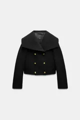 Cazadora corta negra confeccionada en hilatura con lana. Tiene cuello solapa amplio, manga larga, bolsillos delanteros ocultos en costura, forro interior a tono y cierre frontal cruzado con botones metálicos dorados.