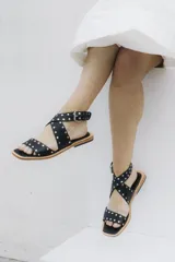 Sandalia de cuero color tostado con adornos de tachas y un diseño elegante y moderno.