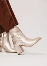 Bota de caña media color champagne de cuero, con horma redonda, taco cuadrado y pequeña plataforma. Cuenta con cierre del lado interno.