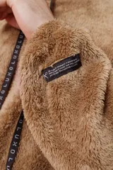 Hoodie beige de piel de corderito sintético, corte oversize con cierre central al estilo anorak, capucha con cordón ajustable y bolsillo canguro.