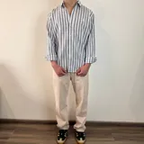 Camisa de manga larga a rayas verticales grises y blancas, con cuello clásico y cierre frontal con botones.