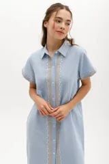 Vestido largo de lino en color celeste, con cuello camisero, manga corta y cierre frontal con botones. Presenta bordados decorativos en contraste en la pechera y en el ruedo.