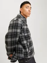 Sobrecamisa corta de manga larga con cuello sport, cierre frontal de cremallera, puños con botones, solapa cortaviento, bolsillos en pecho y delanteros. Diseño a cuadros grises y negros.