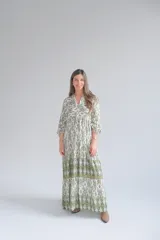 Vestido largo color blanco con estampado geométrico en verde y ocre. Tiene cuello mao, mangas largas abullonadas y corte imperio con falda escalonada.
