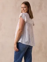 Blusa color marrón claro de algodón con bordados y calados blancos. Tiene cuello a la base, escote en V con lazo de ajuste y mangas cortas amplias.