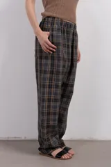 Pantalón largo de corte amplio con estampa escocesa en tonos grises, marrones y blancos. Tiene cintura elástica y tejido suave al tacto.