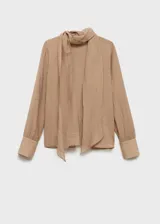 Blusa color beige con textura, cuello alto con lazo, mangas largas con puños abotonados y corte recto.
