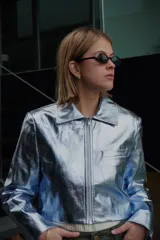 Chaqueta corta plateada con cierre frontal, cuello camisero y mangas largas.