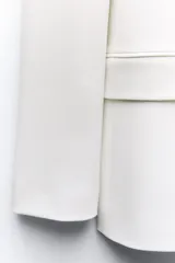 Blazer color blanco hueso, de corte entallado y doble botonadura dorada. Tiene cuello con solapa, mangas largas con hombreras y bolsillos delanteros con solapa.