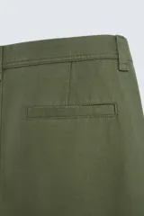 Pantalón chino color verde militar, de corte recto, con bolsillos laterales y traseros de vivo. Cierre frontal con cremallera y botón.