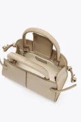 Bolso mini city color beige con doble asa de mano y asa bandolera extraíble. Tiene detalles laterales, pespuntes en el cuerpo y cierre con solapa y botón imantado.