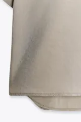Camisa azul de cuello solapa y manga corta con dobladillo. Tiene dos bolsillos de parche en el pecho, bajo asimétrico con aberturas laterales y cierre frontal con botones ocultos.