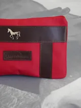 Sobre tipo cartuchera color borgoña, de lona con terminaciones en cuero marrón. Tiene cierre superior y aplique de cuero con el logo de la marca.