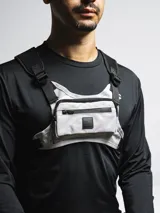 Bolso de pecho táctico color gris claro con detalles en negro. Posee un compartimento principal con cierre y correas ajustables negras para llevar cruzado sobre el pecho.