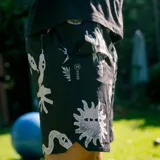 Bermuda negra con estampado de serpientes, soles y cactus en blanco. Confeccionada en poliéster reciclado REPREVE® con acabado DWR resistente al agua. Incluye bolsillos laterales, trasero con cierre YKK y lateral con cierre.