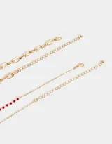 Set de dos collares dorados: uno con cadena de eslabones gruesos y dije de corazón esmaltado en rojo, y otro con cadena de cuentas rojas y dije de strass.
