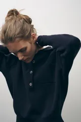 Jersey azul marino de punto liso, con cuello polo, manga larga, bolsillo de parche en el pecho y cierre frontal con botones.