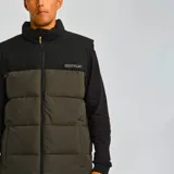 Chaleco acolchado Caterpillar, color marrón con parte superior negra, cierre frontal con cremallera, cuello alto y bolsillos laterales con cierre.