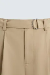 Pantalón negro de corte amplio con cinturón de tela con hebilla metálica. Presenta pliegues frontales, bolsillos laterales y traseros. Cierre frontal con cremallera y botón.