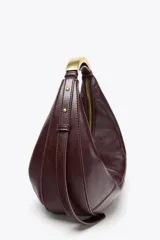 Bolso ovalado color borgoña de cuero sintético, con asa de hombro metálica dorada y cierre de cremallera.