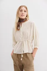 Camisa cruda de algodón jacquard con bordados a tono en el frente y las mangas. Tiene corte a la cintura con lazo interno ajustable, botones frontales y mangas largas con elástico en los puños.