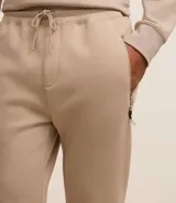 Conjunto deportivo color beige compuesto por un buzo de cuello redondo y un pantalón de jogging con cintura elástica y bolsillos laterales. El buzo es de corte clásico y el pantalón es ajustado en los tobillos.