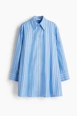 Vestido camisero de corte evasé y holgado, color celeste con finas rayas verticales en negro. Presenta cuello de pico, botonadura frontal y mangas largas con puños abotonados.