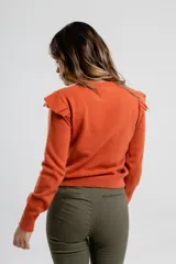 Buzo de punto color naranja con detalles de volantes en los hombros y cuello redondo.