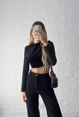 Top corto negro de terciopelo, con cuello alto y mangas largas de tul con lunares plateados.