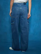 Pantalón de jean de tiro alto, color azul medio, con corte ancho y pierna recta. Presenta costuras marcadas en el centro de las piernas y bolsillos cargo a los lados.