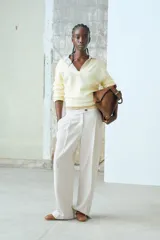 Pantalón sastrero color beige de sarga con pinzas, corte holgado, tiro alto, pretina prolongada con botón, bolsillos al bies y bolsillos insertados atrás. Piernas anchas con pliegues adelante y atrás.