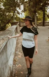 Remera de maternidad color beige con mangas cortas y corte holgado. Presenta un panel horizontal a rayas grises y un sistema de apertura horizontal con telas cruzadas por debajo.