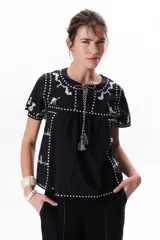 Blusa negra con bordados blancos de animales y motivos geométricos. Tiene cuello redondo con lazo y mangas cortas.